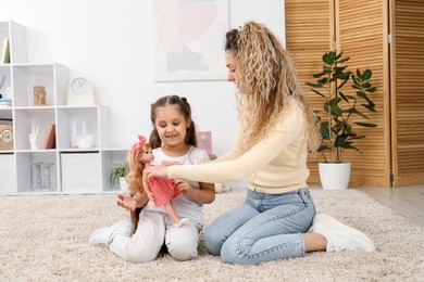 Photo of Mother and her daughter playing with doll on floor at home