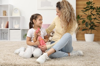 Photo of Mother and her daughter playing with doll on floor at home