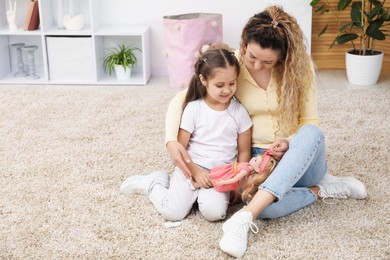 Photo of Mother and her daughter playing with doll on floor at home