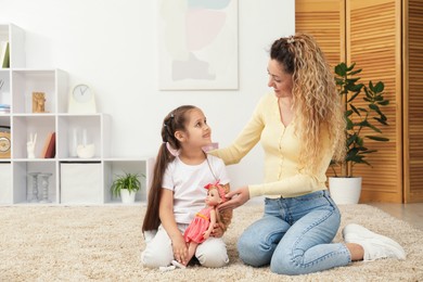 Photo of Mother and her daughter playing with doll on floor at home