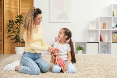 Photo of Mother and her daughter playing with doll on floor at home