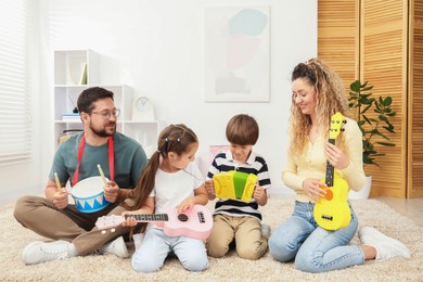 Photo of Parents and their children playing music instruments on floor at home