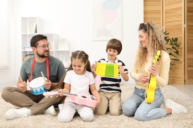 Photo of Parents and their children playing music instruments on floor at home