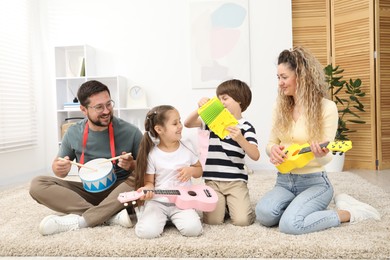 Photo of Parents and their children playing music instruments on floor at home