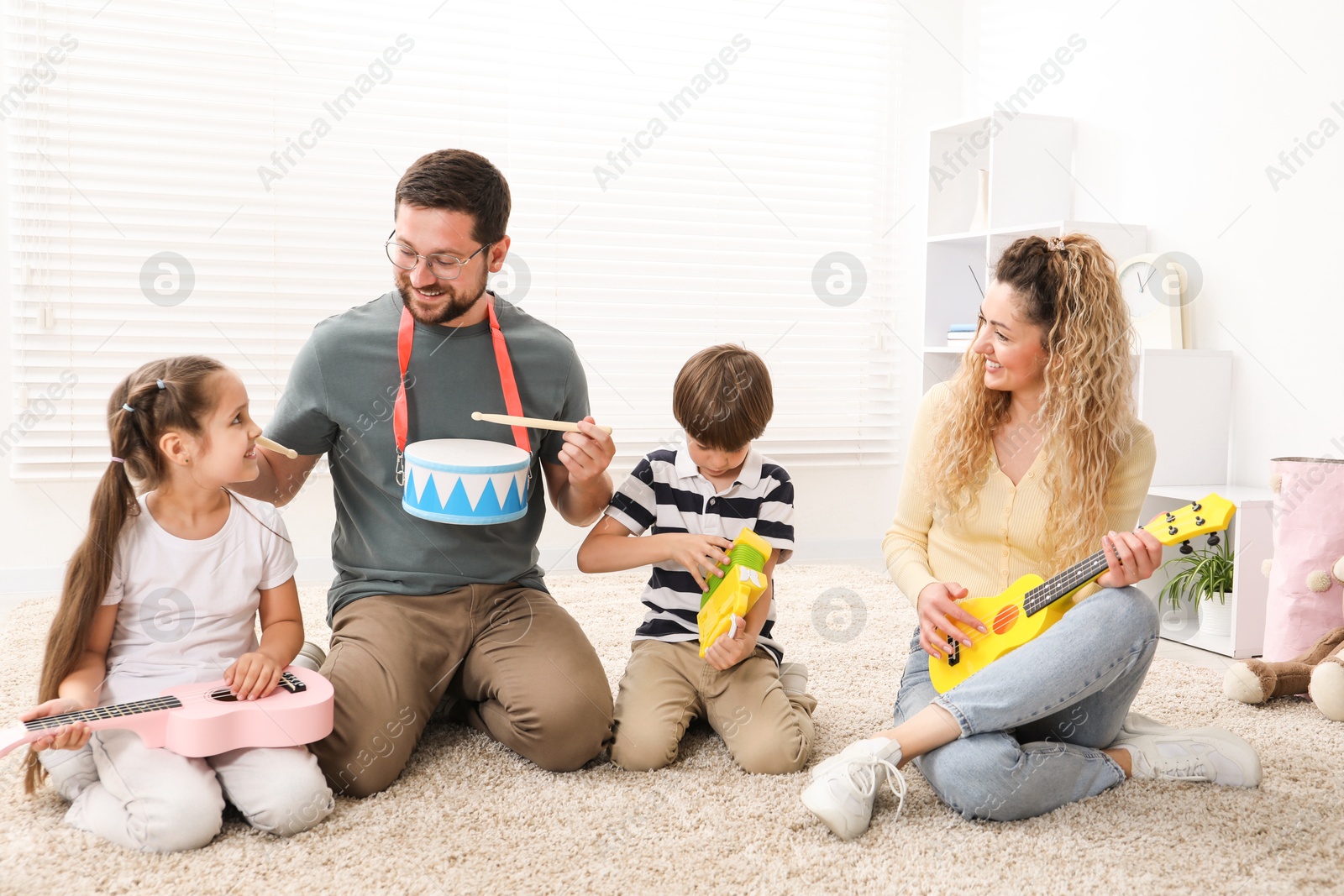 Photo of Parents and their children playing music instruments on floor at home