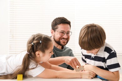 Photo of Father and his children playing with wooden figures at white table indoors