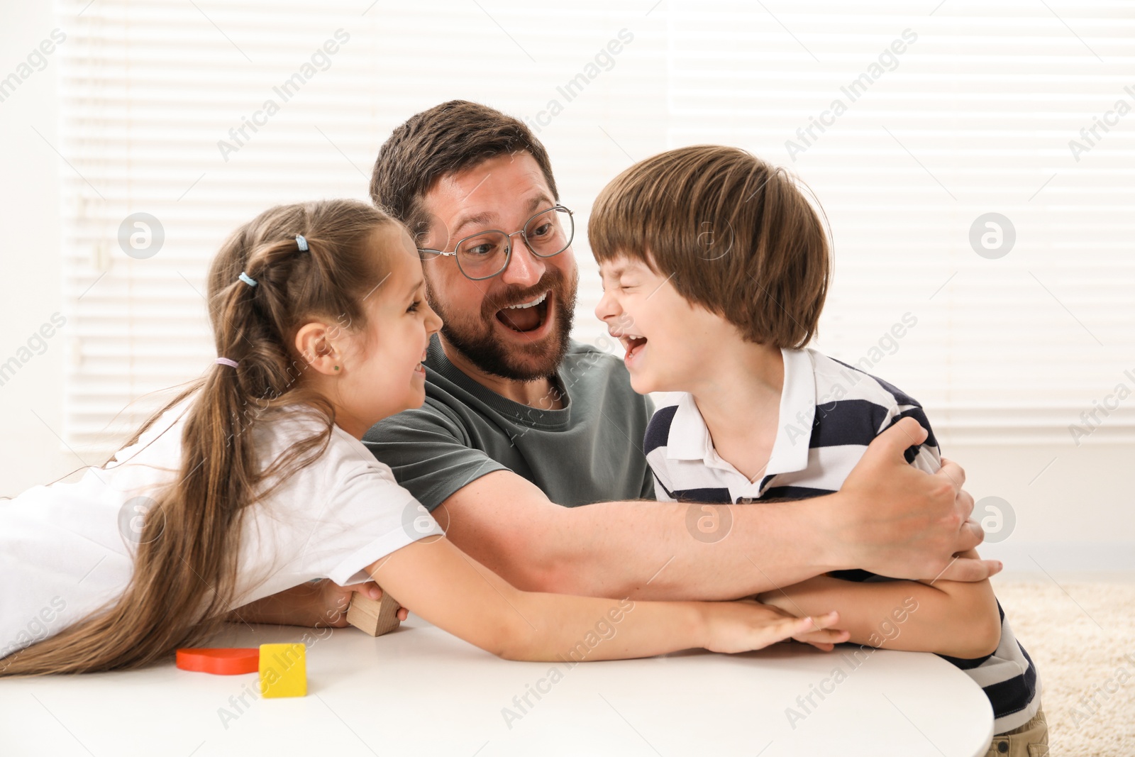 Father and his children playing with wooden figures at white table indoors Photo of Father and his children playing with wooden figures at white table indoors