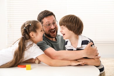 Photo of Father and his children playing with wooden figures at white table indoors