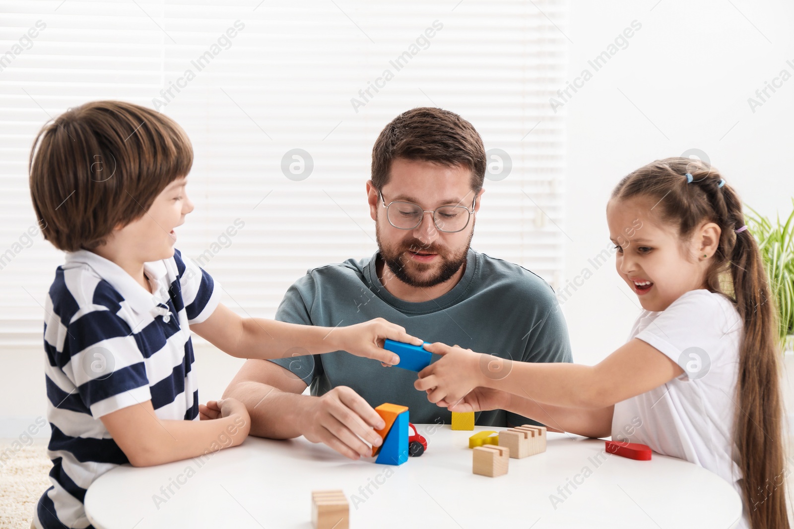 Father and his children playing with wooden figures at white table indoors Photo of Father and his children playing with wooden figures at white table indoors