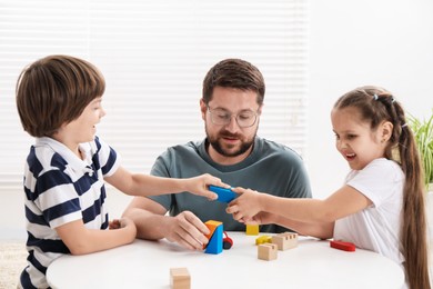 Photo of Father and his children playing with wooden figures at white table indoors
