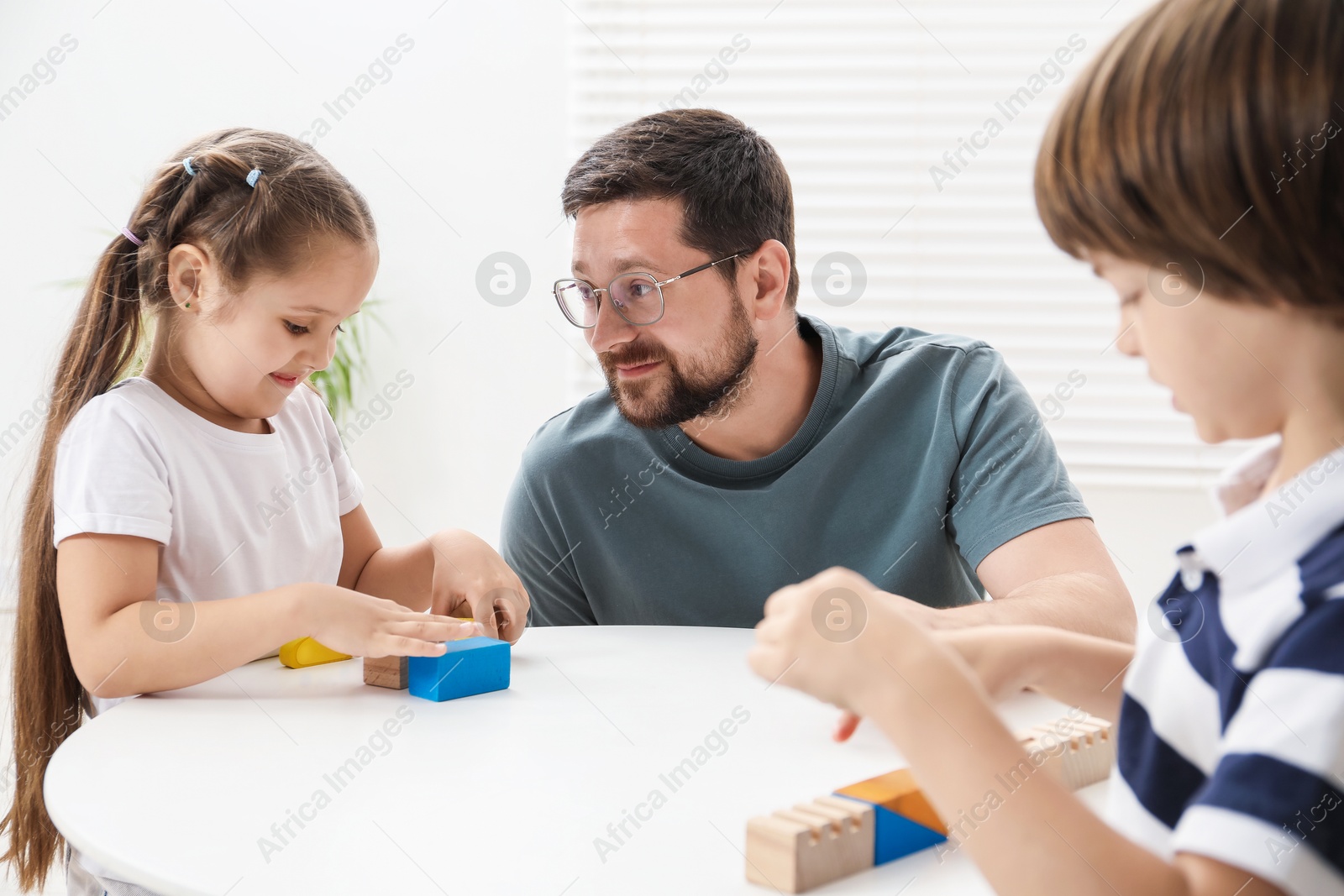 Father and his children playing with wooden figures at white table indoors Photo of Father and his children playing with wooden figures at white table indoors