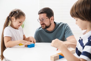 Photo of Father and his children playing with wooden figures at white table indoors