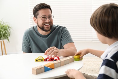 Photo of Father and son playing with wooden figures at white table indoors