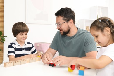 Photo of Father and his children playing with wooden figures at white table indoors