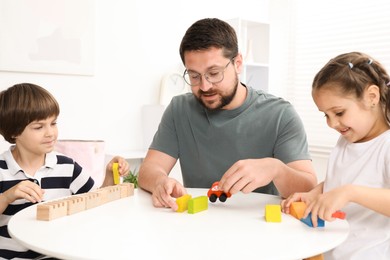 Photo of Father and his children playing with wooden figures at white table indoors