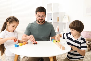 Photo of Father and his children playing with wooden figures at white table indoors