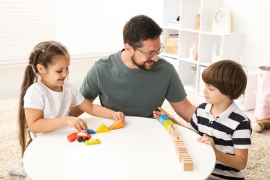 Photo of Father and his children playing with wooden figures at white table indoors