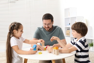 Photo of Father and his children playing with wooden figures at white table indoors