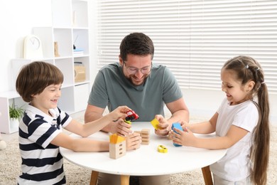Photo of Father and his children playing with wooden figures at white table indoors