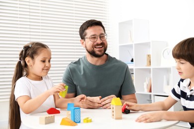 Photo of Father and his children playing with wooden figures at white table indoors