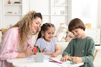 Photo of Mother and her children drawing at white table indoors
