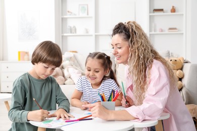 Photo of Mother and her children drawing at white table indoors