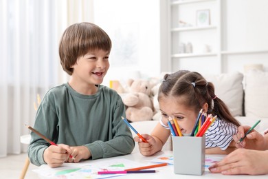 Photo of Children and their mother drawing at white table indoors, closeup