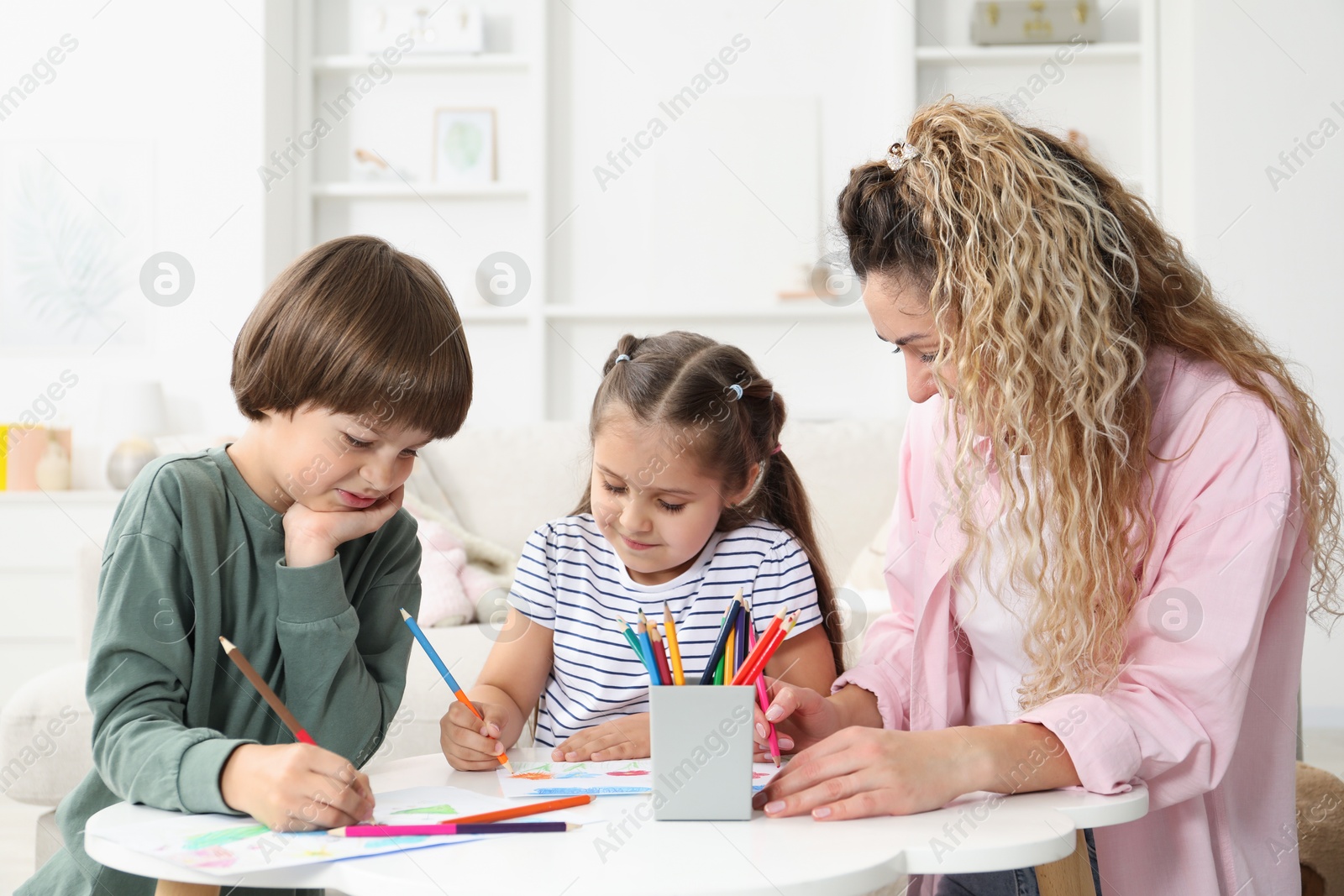 Mother and her children drawing at white table indoors Photo of Mother and her children drawing at white table indoors