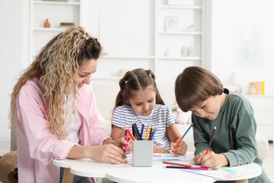 Photo of Mother and her children drawing at white table indoors