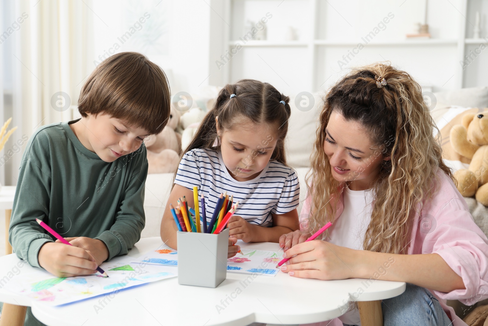 Mother and her children drawing at white table indoors Photo of Mother and her children drawing at white table indoors