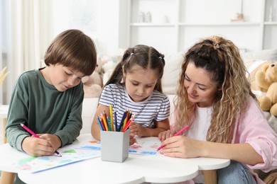 Photo of Mother and her children drawing at white table indoors