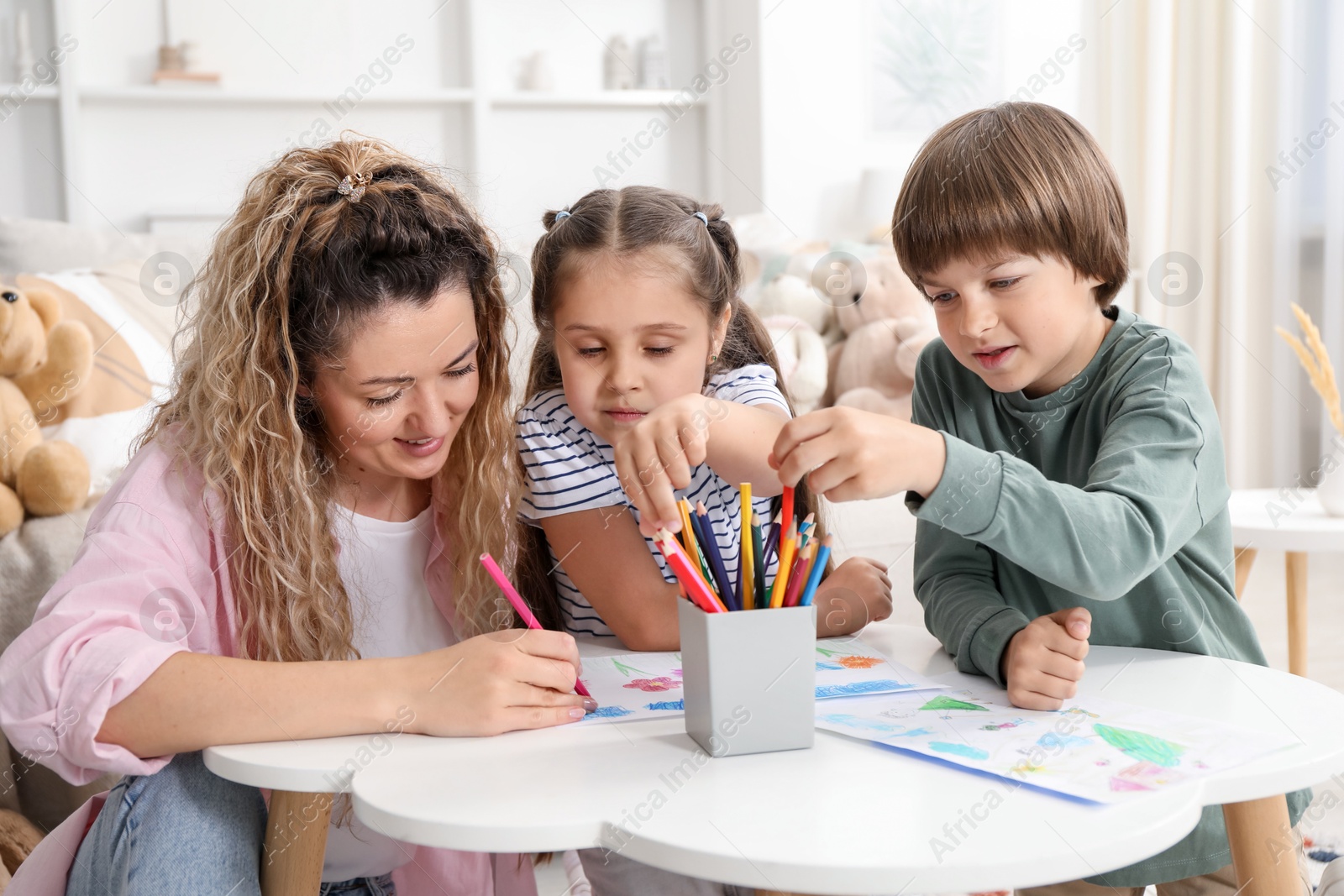 Photo of Mother and her children drawing at white table indoors