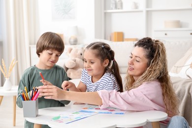 Photo of Mother and her children drawing at white table indoors