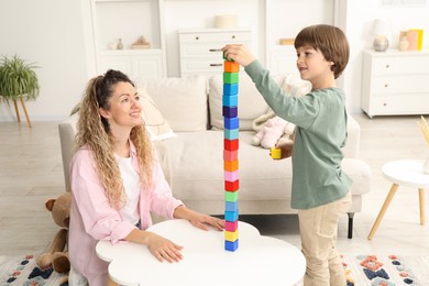 Photo of Mother and her son building tower with wooden cubes at white table indoors