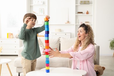 Photo of Mother and her son building tower with wooden cubes at white table indoors