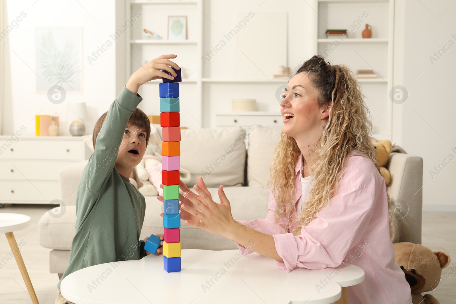 Mother and her son building tower with wooden cubes at white table indoors Photo of Mother and her son building tower with wooden cubes at white table indoors