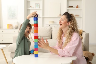 Photo of Mother and her son building tower with wooden cubes at white table indoors