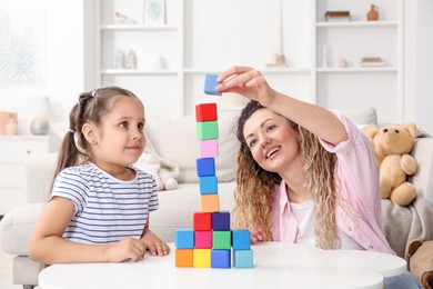 Photo of Mother and her daughter building tower with colorful cubes at white table indoors