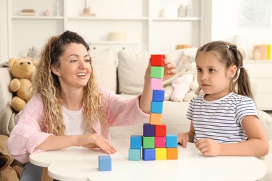 Photo of Mother and her daughter building tower with colorful cubes at white table indoors