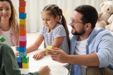 Photo of Children and their parents building tower with colorful cubes at white table indoors