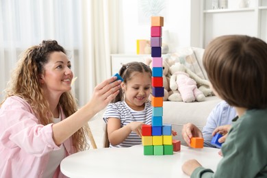 Photo of Children and their parents building tower with colorful cubes at white table indoors
