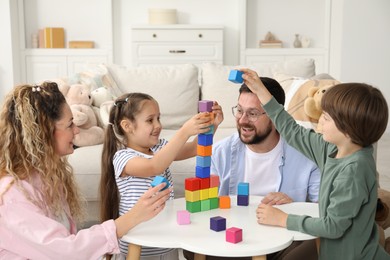 Photo of Children and their parents building tower with colorful cubes at white table indoors