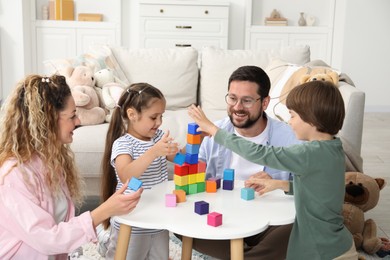 Photo of Children and their parents building tower with colorful cubes at white table indoors
