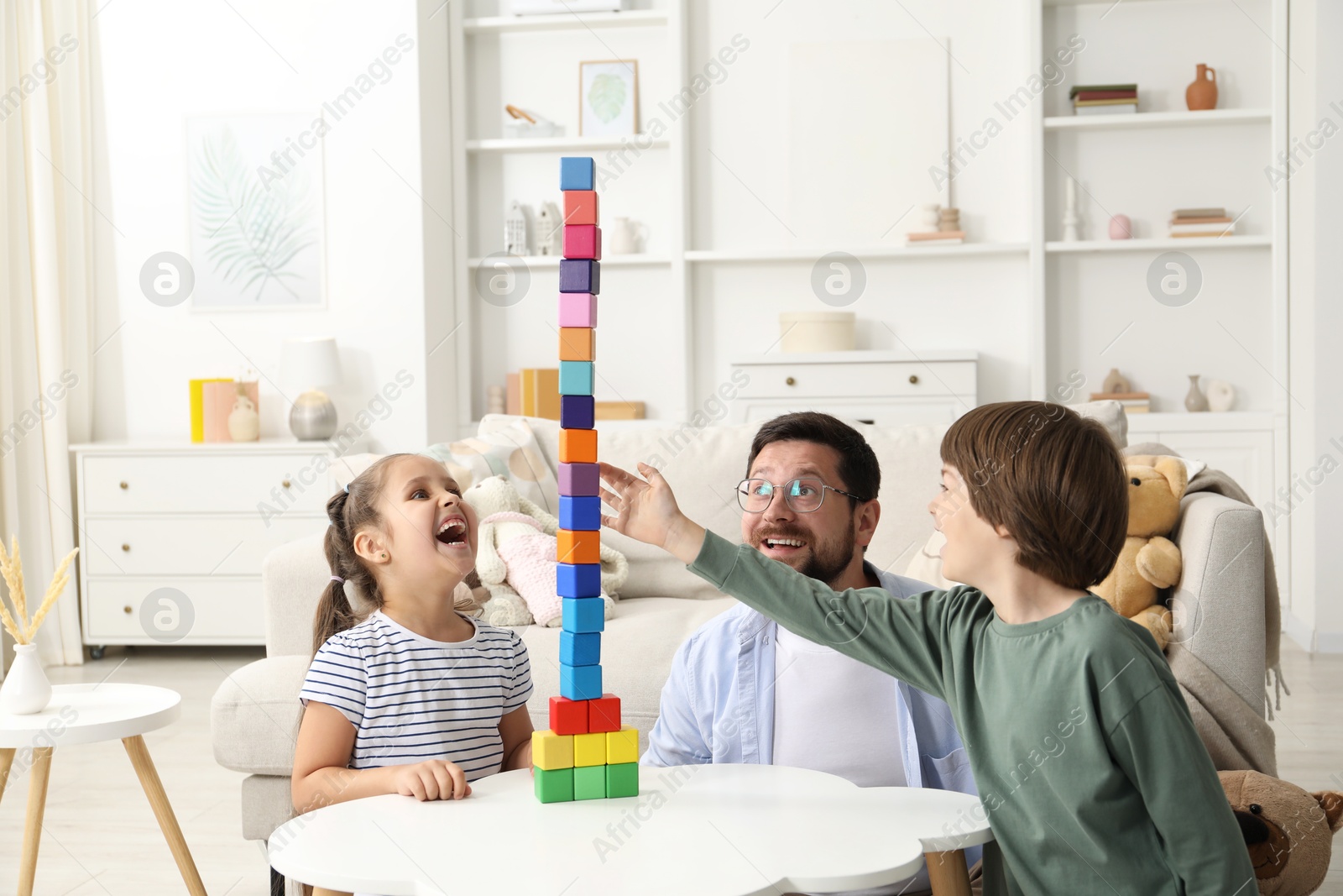 Children and their father building tower with colorful cubes at white table indoors Photo of Children and their father building tower with colorful cubes at white table indoors