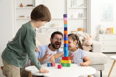 Photo of Children and their father building tower with colorful cubes at white table indoors