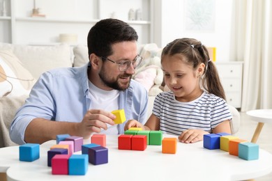 Photo of Father and his daughter playing with colorful cubes at white table indoors