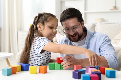 Photo of Father and his daughter playing with colorful cubes at white table indoors