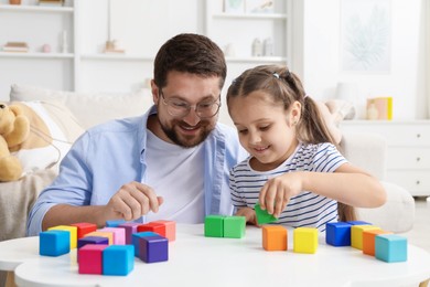 Photo of Father and his daughter playing with colorful cubes at white table indoors