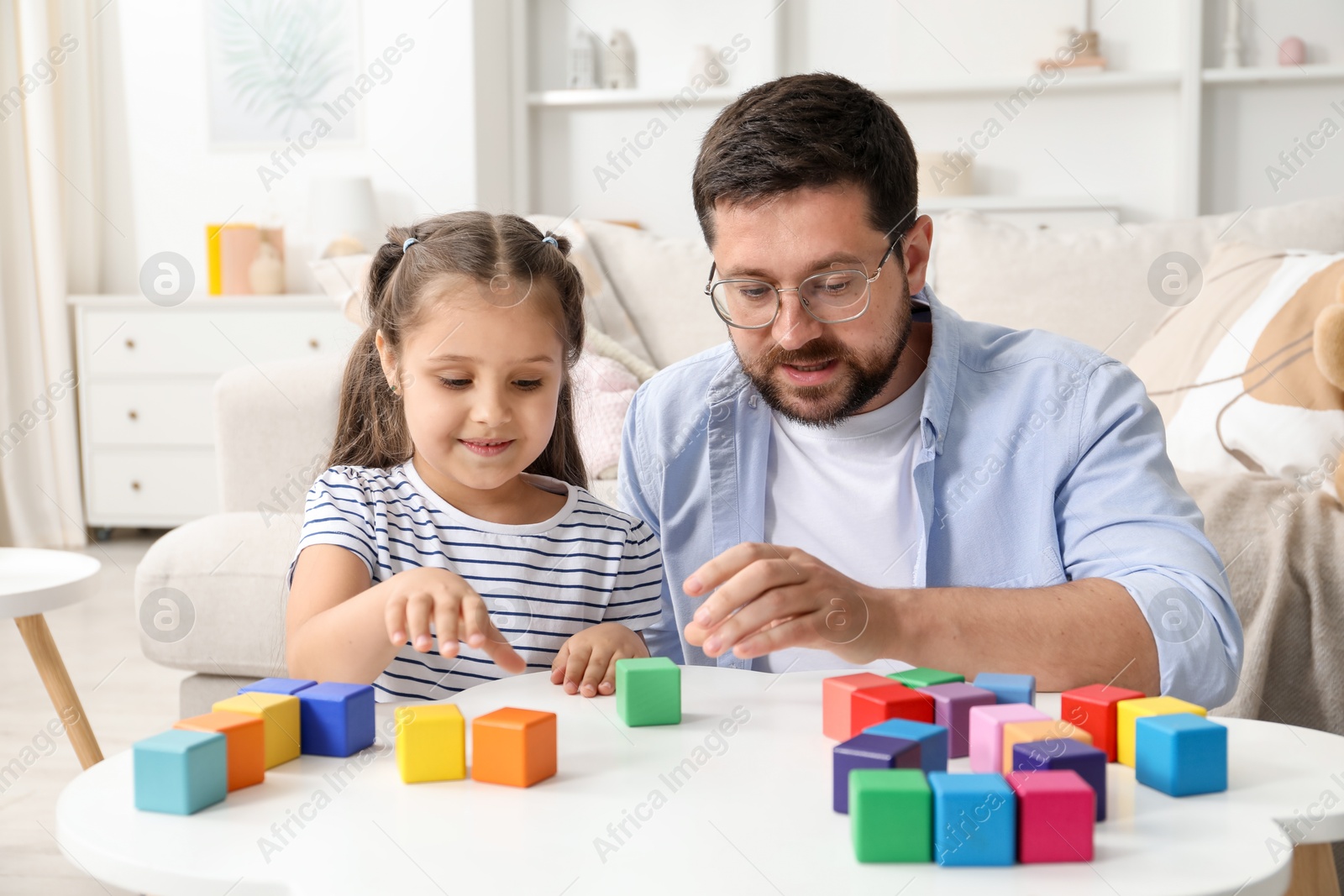 Father and his daughter playing with colorful cubes at white table indoors Photo of Father and his daughter playing with colorful cubes at white table indoors