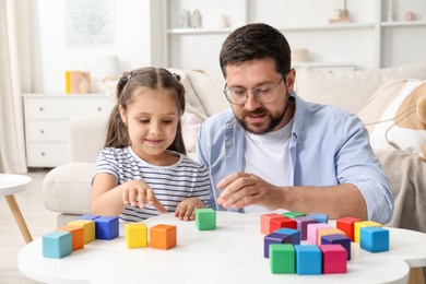 Photo of Father and his daughter playing with colorful cubes at white table indoors